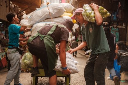 Trabalhadores carregam um carrinho com produtos em um movimentado mercado de rua.