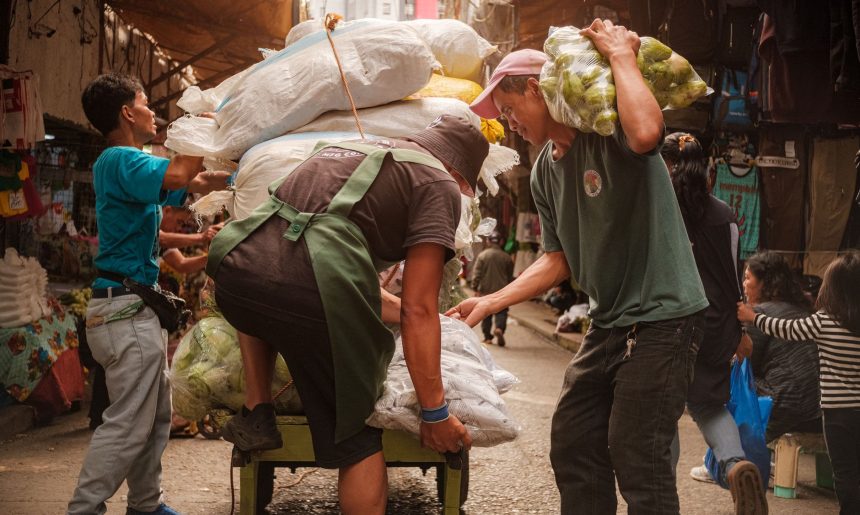 Trabalhadores carregam um carrinho com produtos em um movimentado mercado de rua.