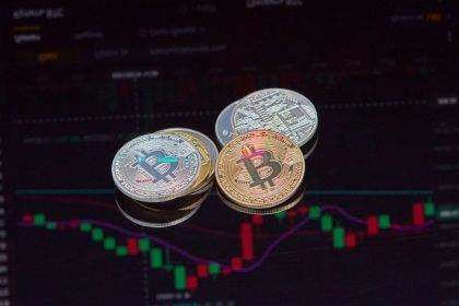 Moedas de Bitcoin em primeiro plano sobre um gráfico de mercado financeiro.